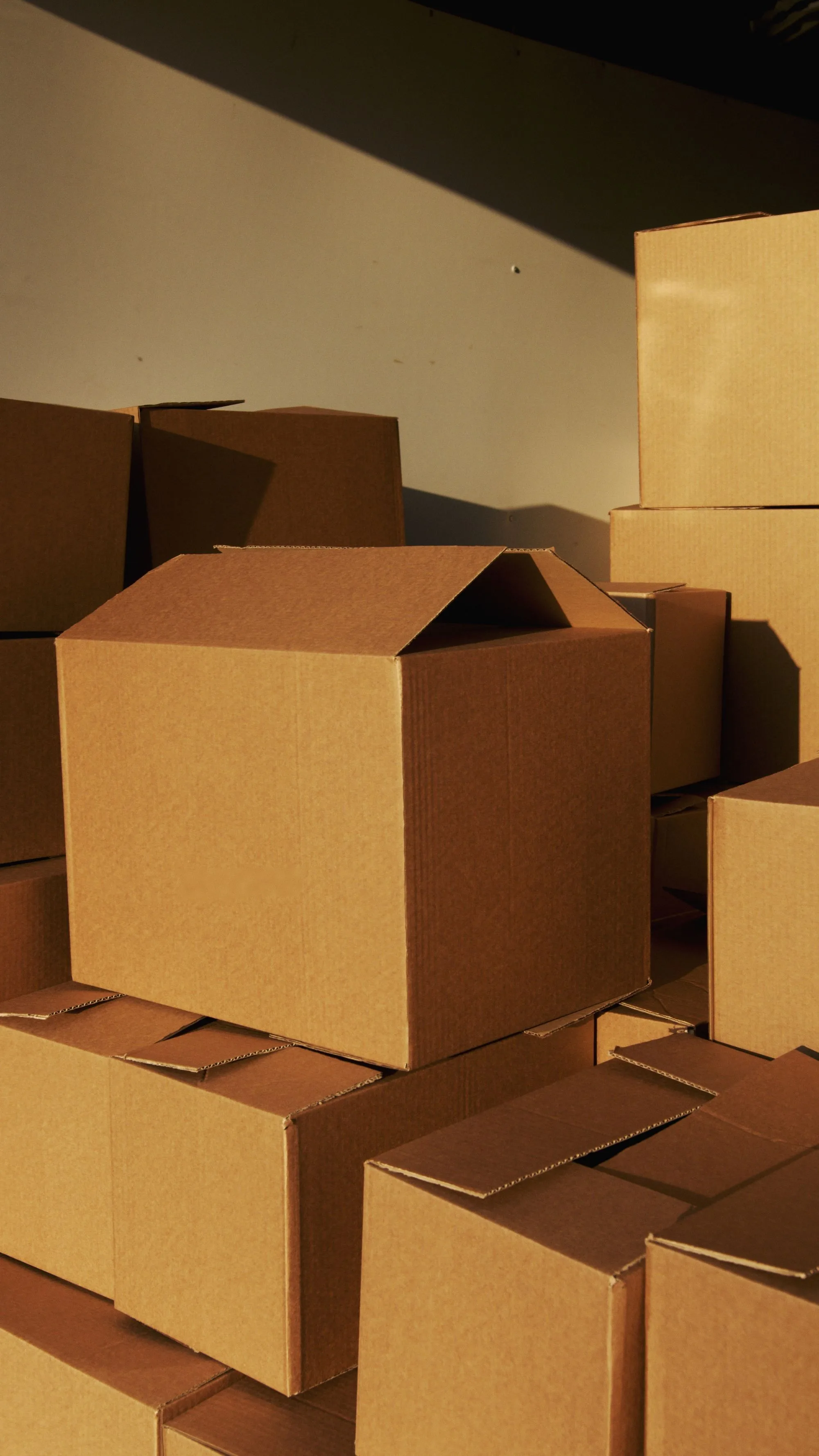 A group of unprinted corrugated cartons stacked under warm directional light