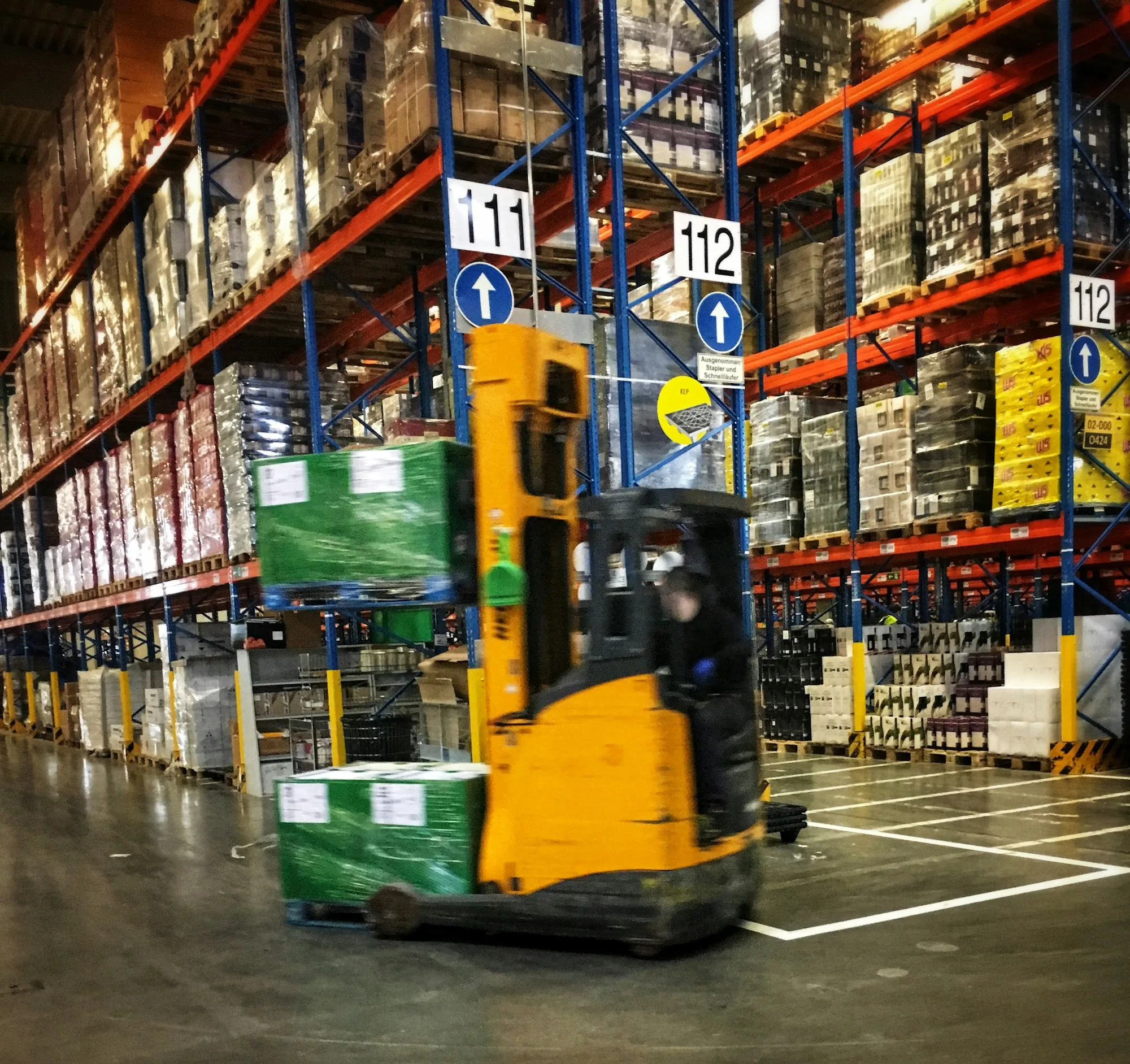 Forklift carrying a wrapped pallet through a working warehouse
