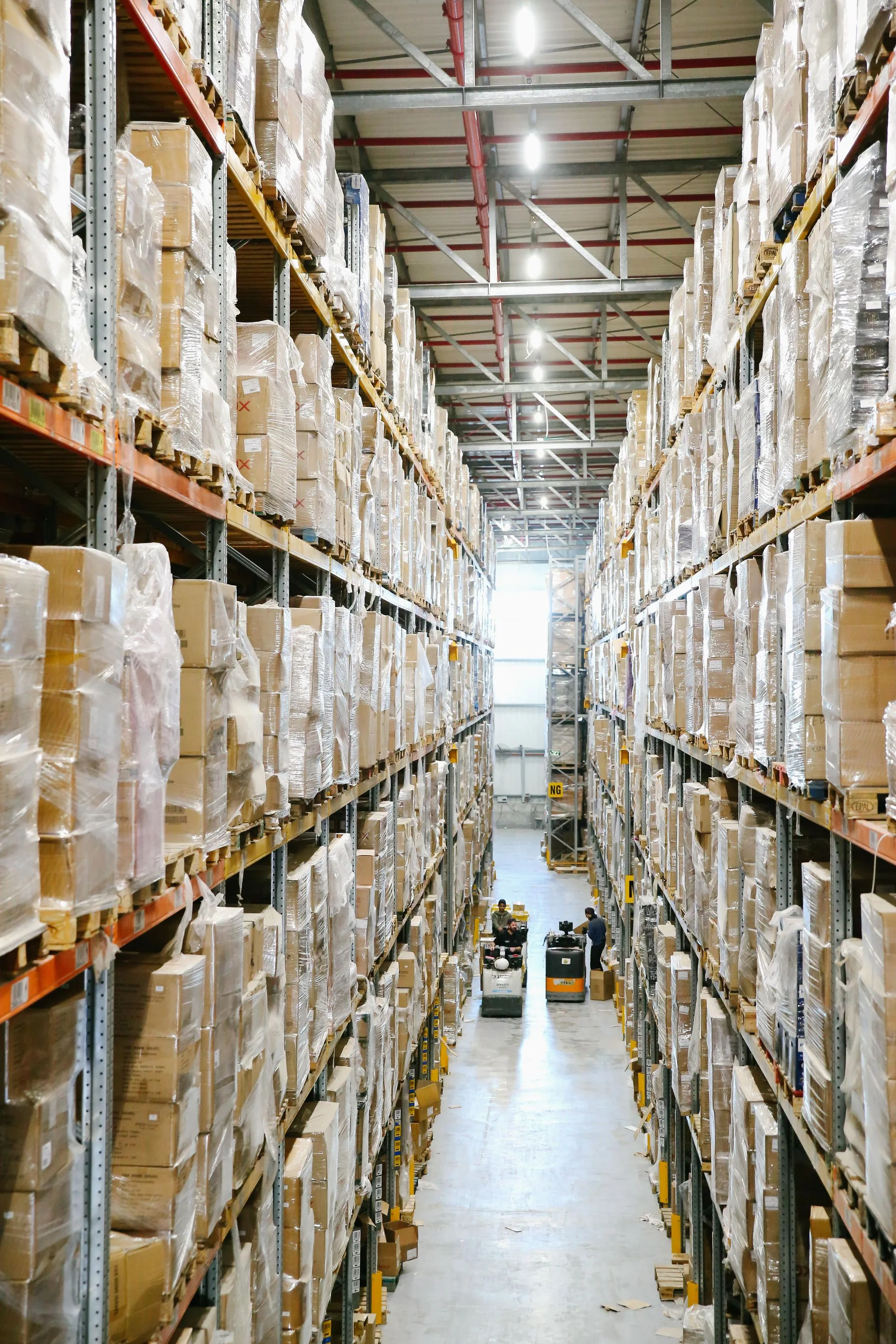 A high-bay warehouse aisle containing wrapped cartons on pallets